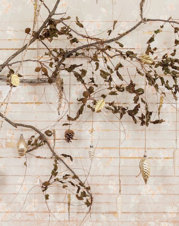 Vintage gold ornaments hanging from branch against rustic white wall.